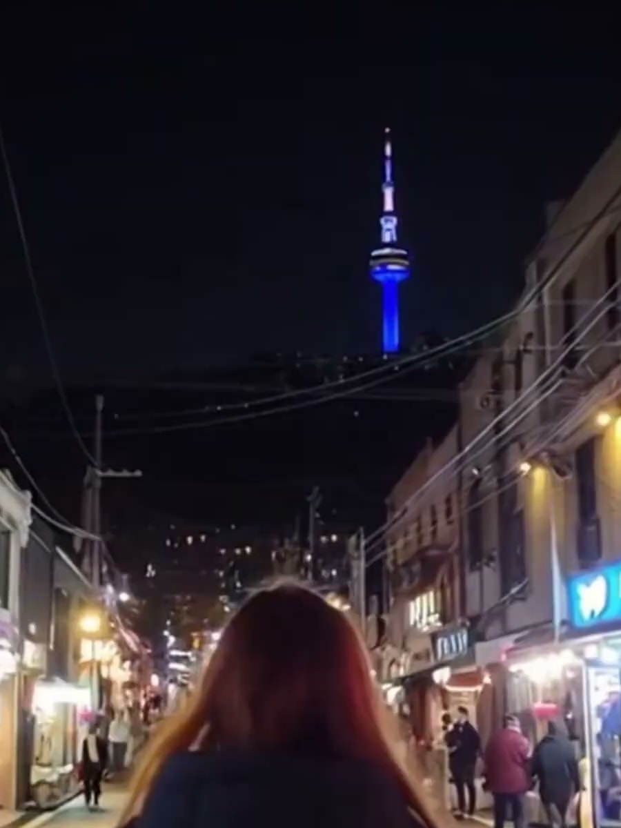 밤거리를 걸어 서울타워가 보이는 언덕 쪽으로 향하는 크리에이터의 뒤를 따라가는 세로 콘텐츠 장면