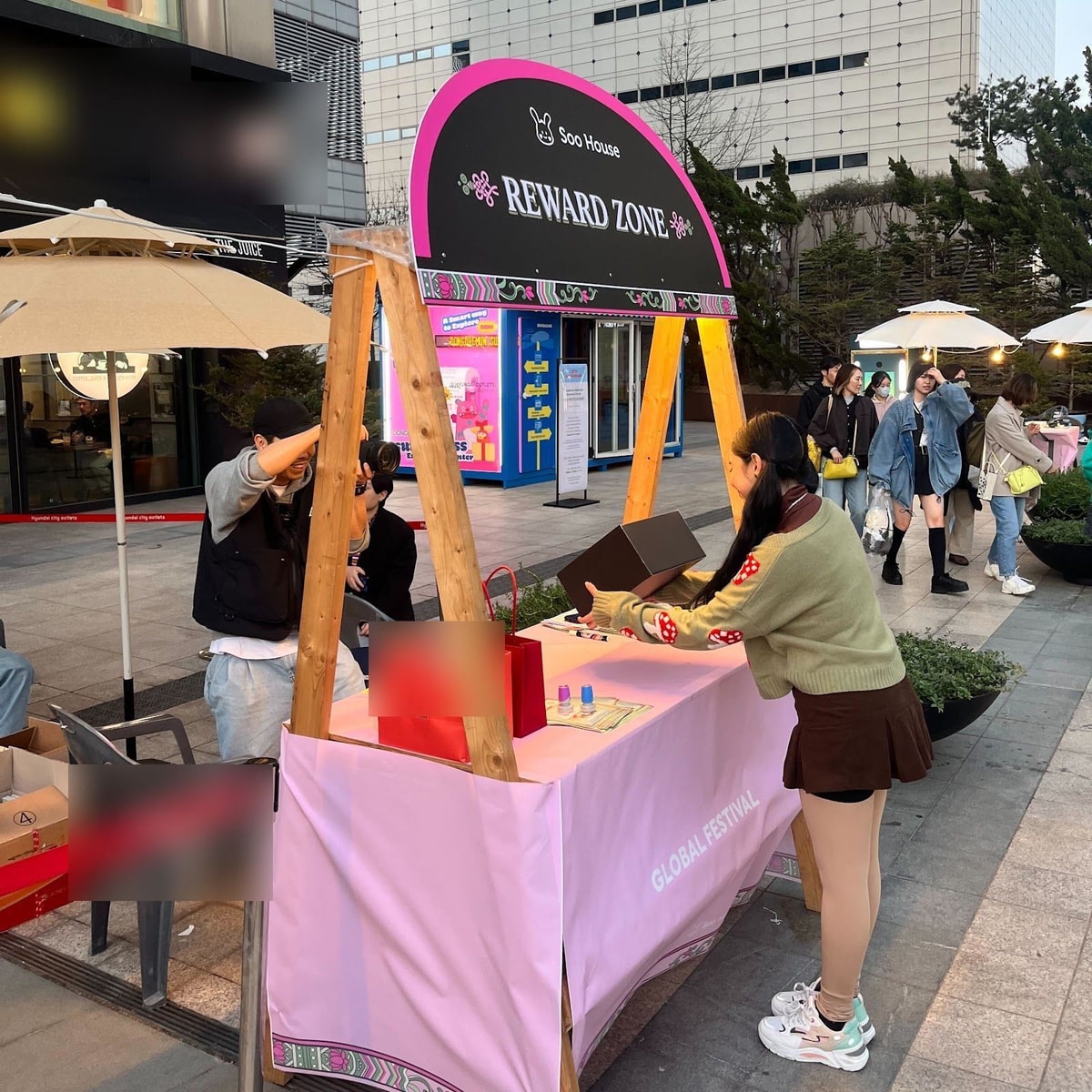 야외 광장에 세운 리워드 존 아치 아래 분홍 테이블에서 스태프가 선물 박스를 정리하는 모습