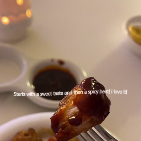 포크로 집어 든 양념 요리 클로즈업. 화면에 단맛 뒤에 매운맛이 온다는 영어 자막이 떠 있고 뒤로 간장 종지가 보인다