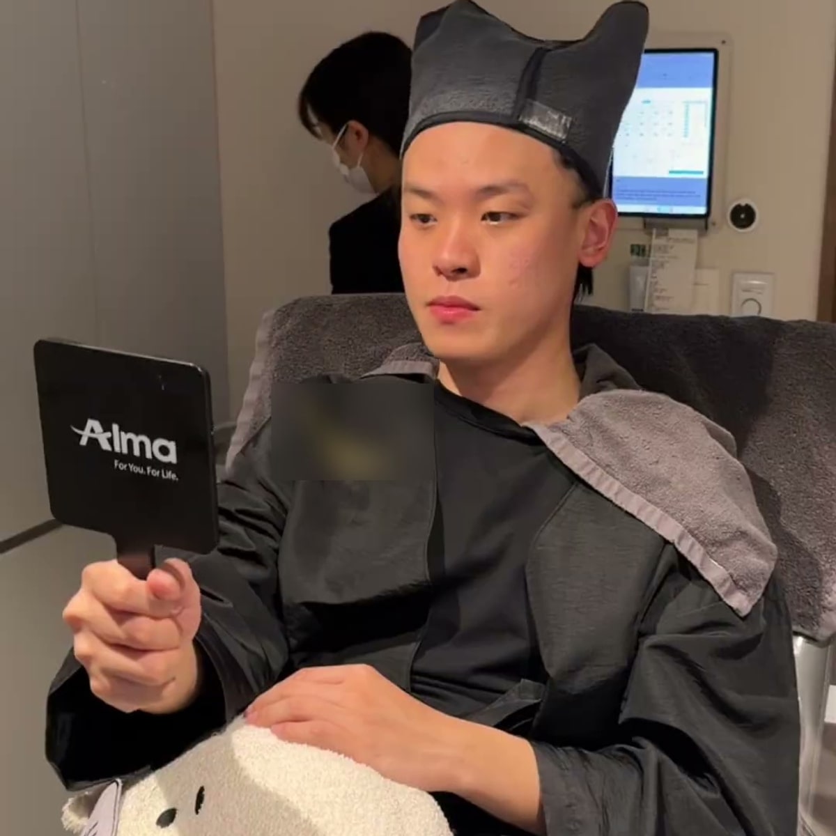 시술 가운을 입은 크리에이터가 진료 의자에 앉아 손거울로 얼굴을 확인하는 모습