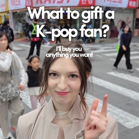 'What to gift a K-pop fan?' 영어 자막이 큼직하게 얹힌 명동 거리 숏폼 표지 — 크리에이터가 브이 손동작을 하고 뒤로 상점 간판과 행인이 보입니다
