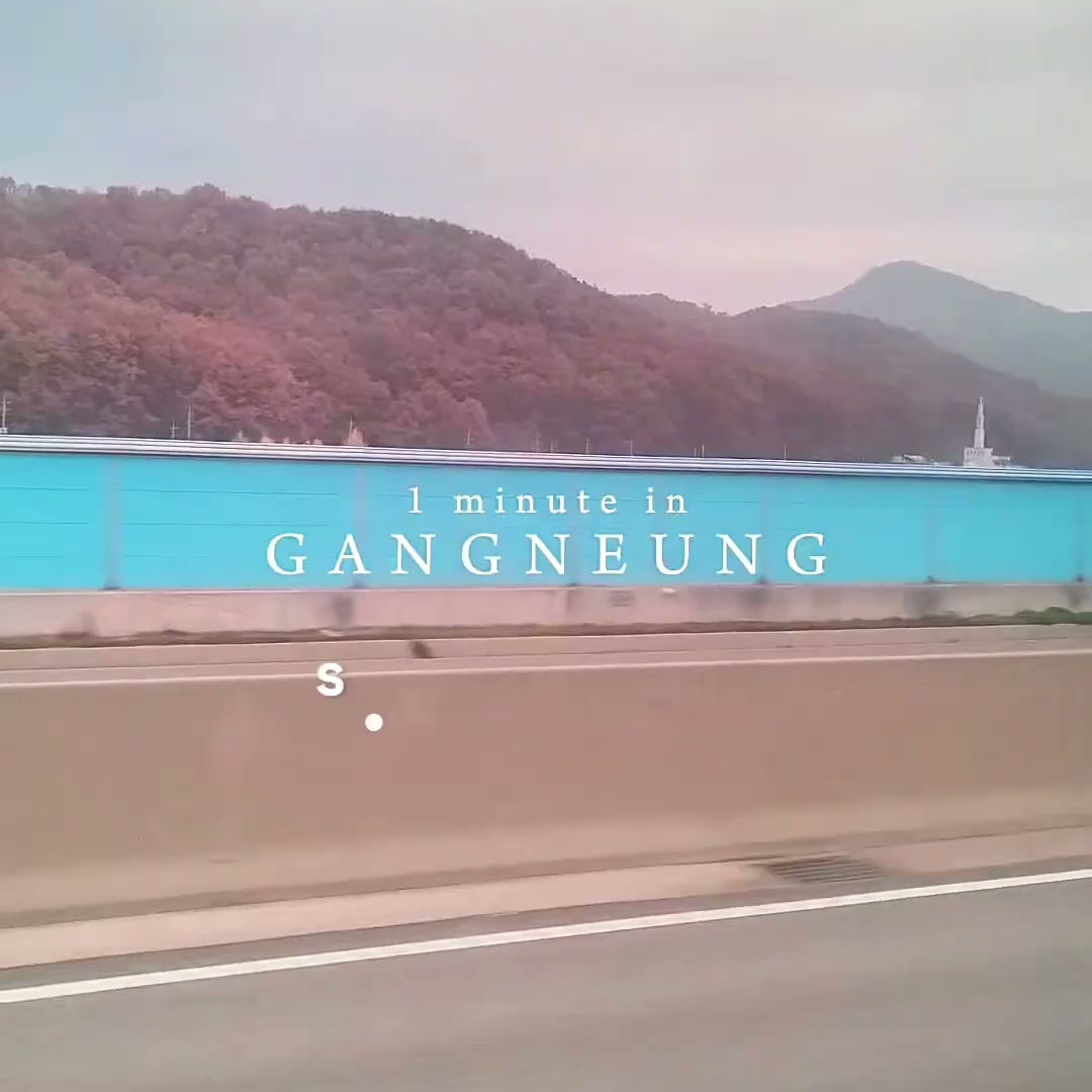 달리는 차 안에서 촬영한 도로와 산 풍경 위에 강릉에서의 1분이라는 영어 자막이 떠 있는 장면