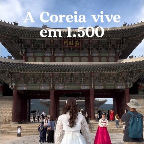 한복을 입은 참가자가 경복궁 흥례문 앞 계단을 향해 걸어가는 뒷모습. 화면 위쪽에 포르투갈어로 “A Coreia vive em 1.500”이라는 자막이 있고 주변에는 관람객들이 지나가고 있다
