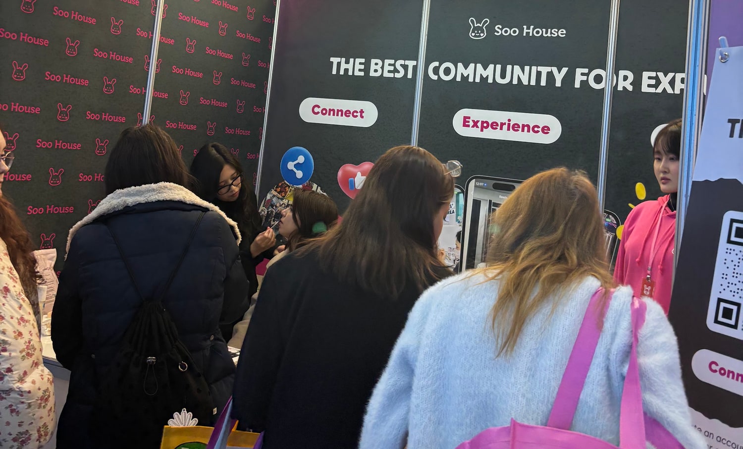 행사장에 설치된 Soo House 부스 앞에 여러 사람이 등을 보인 채 모여 있고, 뒤쪽 배너에 THE BEST COMMUNITY FOR EXPATS 문구가 보인다