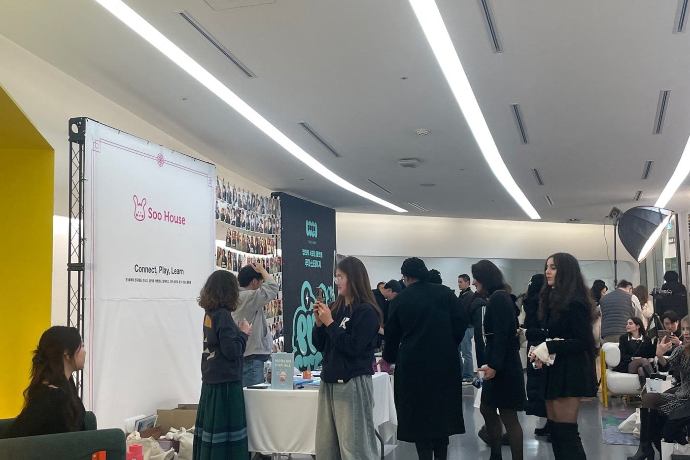 실내 팝업 행사장에서 Soo House 배너 옆 테이블에 안내물이 놓여 있고, 방문객들이 그 주변에 서 있는 장면