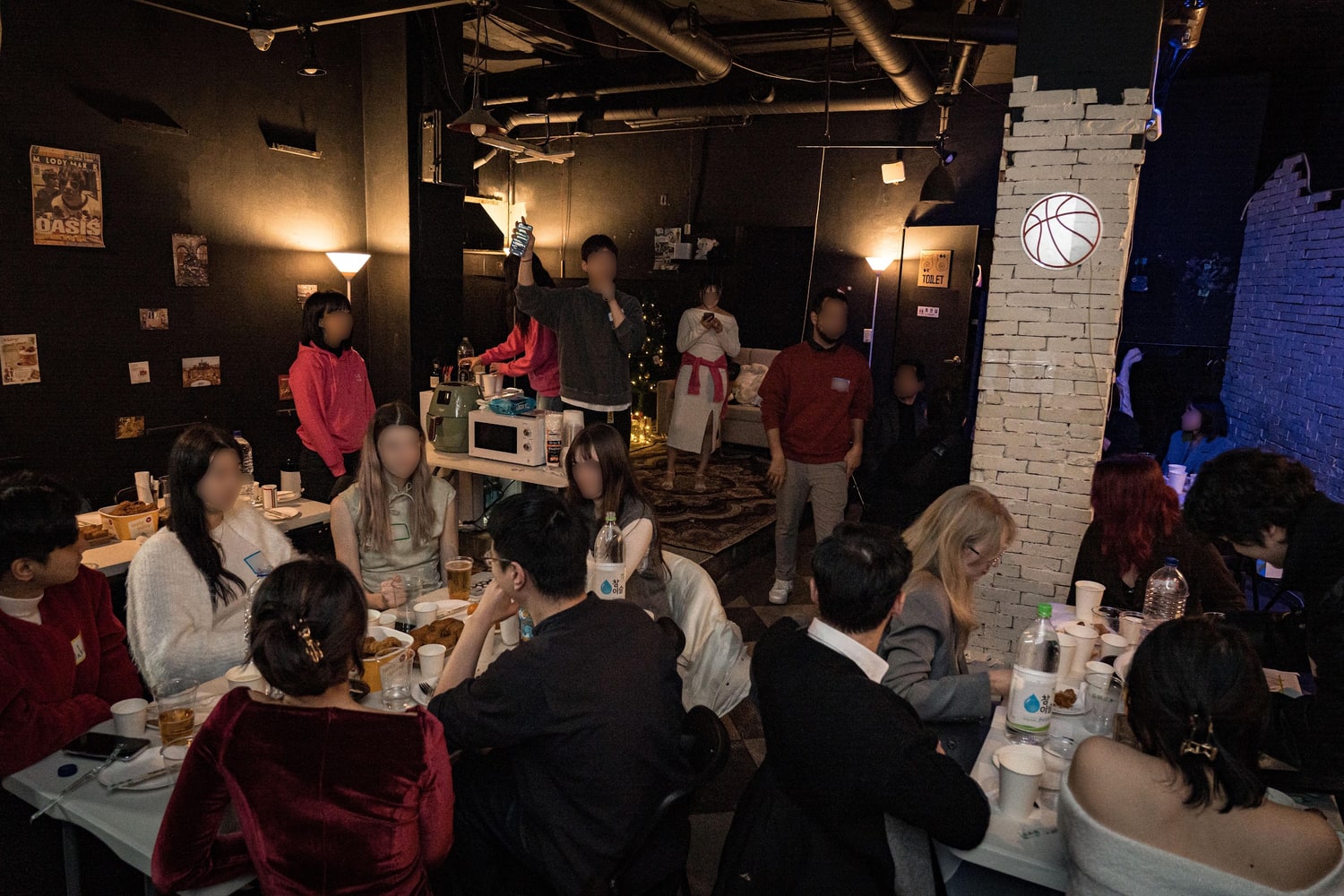 어두운 실내 행사장에서 여러 개의 긴 테이블에 둘러앉아 이야기를 나누는 참가자들. 얼굴은 원본에서 흐리게 처리돼 있다.