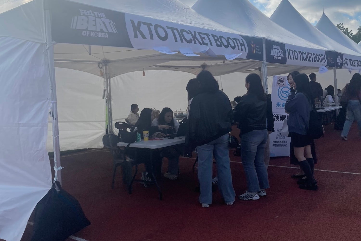 K-팝 콘서트 행사장에 설치된 한국관광공사 티켓 부스. 천막 처마에 KTO TICKET BOOTH 라고 적혀 있고, 오른쪽 안내판에는 중국어 문구가 보인다.