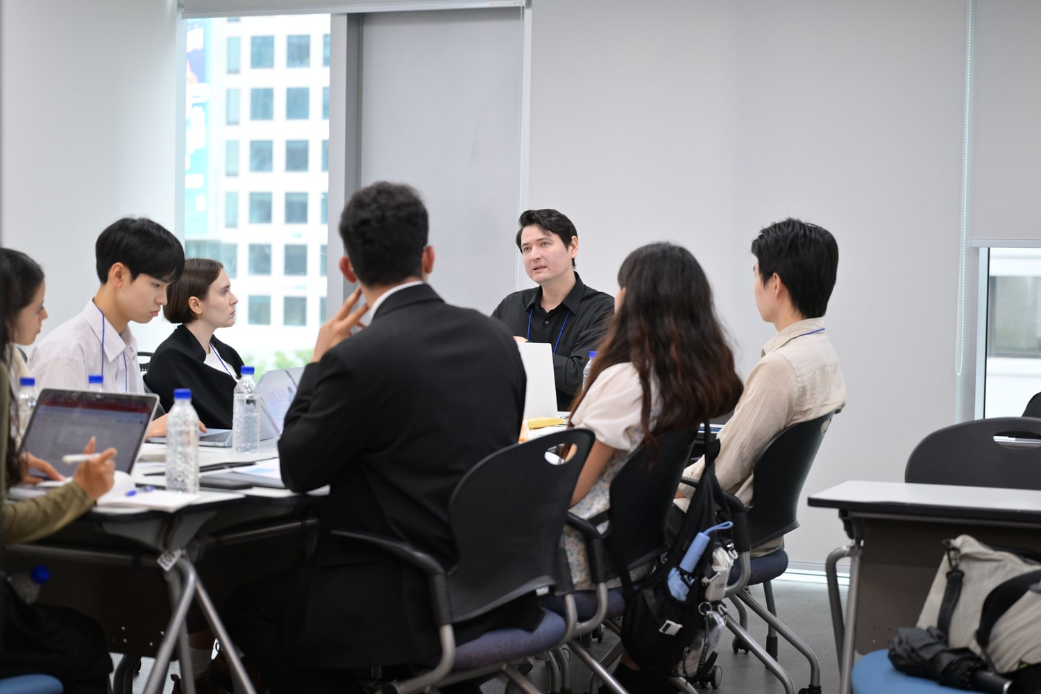 회의실 테이블에 둘러앉은 참가자들이 멘토의 설명을 듣고 있는 모습